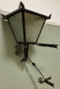 An early 20th century wrought iron wall lamp, pitched top over four frosted glass panes, scrolled