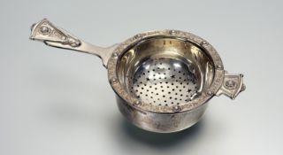 A Birmingham silver loose leaf tea strainer with dish stand and chased Celtic knot and targe
