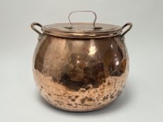 A large copper lidded pot with hammered finish, complete with shaped loop handles to sides and