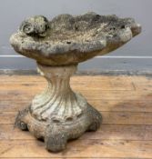 A weathered composition stone bird bath, the bowl modelled as a scallop shell on a swept baluster