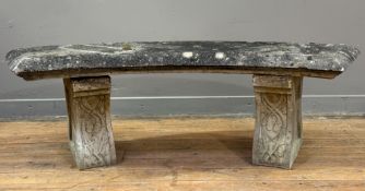 A weathered carved stone curved garden bench in a Neoclassical style, the seat raised on a pair of
