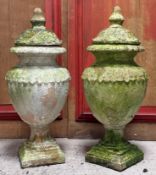 A pair of weather painted ceramic covered garden urns, each domed cover with moulded foliate