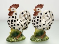 A pair of 20thc Rooster figures, with black polka dots on white to body, on a grassy base.