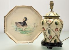 A decorative ceramic table lamp, with a tree and fern pattern, mounted on a circular wooden base (
