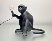 A Seletti Italian moulded resin monkey table lamp, modelled seated holding a bulb bulb, marked to
