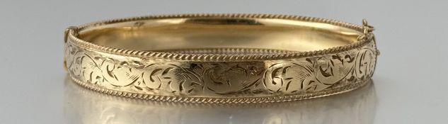 A 9ct gold metal core engraved, stiff hinged bangle with clip fastening and safety chain with rope