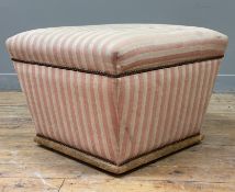 An early 20th century upholstered ottoman footstool, covered in pink striped fabric with brass