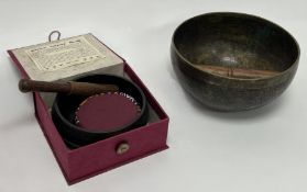 A Tibetan bronze singing bowl with wooden beater, presented within an embossed red case (d. bowl