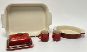 A collection of Le Creuset stoneware dishes in red tones, comprising a twin-handled rectangular