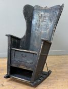 A vernacular pine lambing chair by Ramsay Gillies, stained pine wingback and plank seat, storage