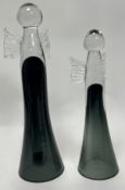 A graduated pair of hand-blown dark green glass decorative angel figurines, raised on conical