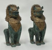A pair of patinated cast metal temple guardian lion statues with gilt decoration to the head and