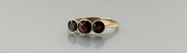 A gold three stone graduated garnet ring, centre stone approximately 0.75ct Q 2.4g