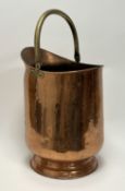 A copper coal scuttle, raised on a circular base with a brass swing handle (h. 50cm)