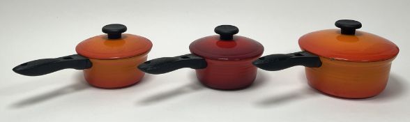 A collection of three Le Creuset cast iron saucepans with covers, two in the 'Flame Orange' hue, the
