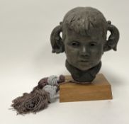 A handmade mixed media bust of a child with pigtails, with bronzed patinated effect and raised on