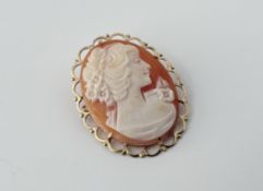A 9ct gold modern shell carved oval portrait cameo brooch/ pendant within a scrolling framed border: