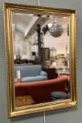 A modern gilt-framed wall-hanging mirror with moulded scroll detail and beaded border (85cm x 60cm)