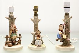 A group of three Goebel Hummel porcelain figurine table lamps, one of a girl seated on a fence (a/