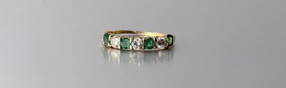 A seven stone diamond and emerald ring, the uniform band of alternating stones claw-set on an 18ct