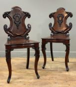 A pair of 19th century mahogany hall chairs, each with cartouche-shaped scroll-carved back, on