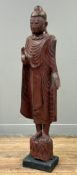 A South-East Asian red-lacquered carved wooden figure of a standing Buddha, c.1920-30, the right