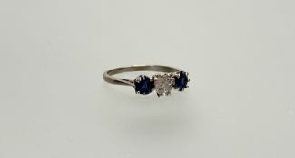 A three-stone sapphire and diamond ring, the central round brilliant-cut diamond claw-set between