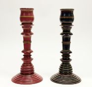 A pair of Easten style striped ring turned wooden candlesticks on circular stepped base, one red