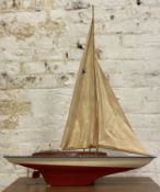 A mid-century model pond yacht, with sails and rigging over teak deck and red hull (a/f): H. 115cm