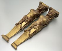 A pair of carved wooden wall brackets, in female body form, in a gold and red paint. (l-57cm) (2)