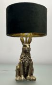 A gold-coloured resin table lamp, the base in the form of a seated rabbit with circular green drum