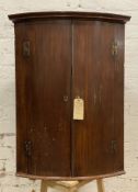 A Georgian mahogany corner cupboard, moulded cornice over twin curved panel doors, enclosing three