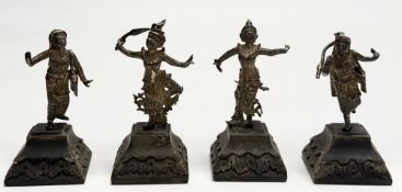 A Thai group of four cast white metal standing figures in various poses mounted on carved hardwood