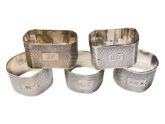 Five various silver napkins rings with engine turned decoration and engraved initials/names