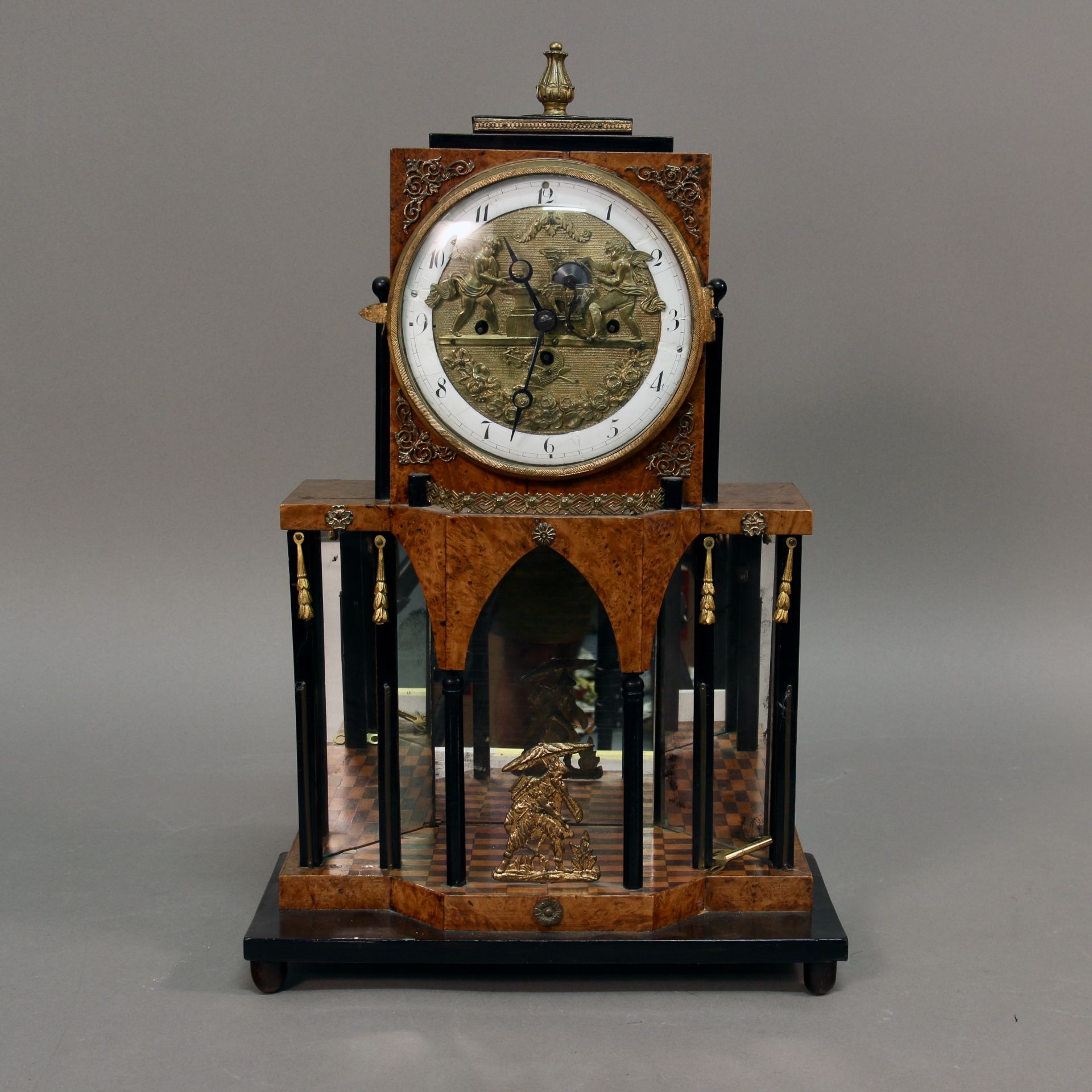 Empire Kommodenuhr "Schmied und Schleifer", um 1800, Wurzelholzfurnier, ebonisierte Säulen, 3-fach