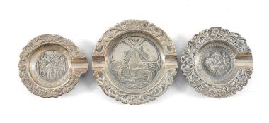 THREE CONTINENTAL CIRCULAR WHITE METAL ASHTRAYS, repoussé decoration of windmill and figures, one
