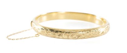 9CT GOLD FOLIATE ENGRAVED HINGED BANGLE, cuff size 60mms, with safety chain, 10.5g Provenance: