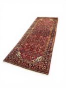 PERSIAN HANDMADE WOOL RUG, red ground with floral centre field within floral border, 288 x 110cms