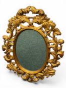 ORNATE GILT FRAMED WALL MIRROR of oval form, pierced and carved with leaves and scrolls, bevelled