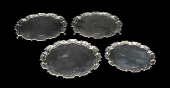 FOUR PIE-CRUST CIRCULAR SILVER WAITERS including pair raised on scrolled feet, Sheffield 1978, 15.