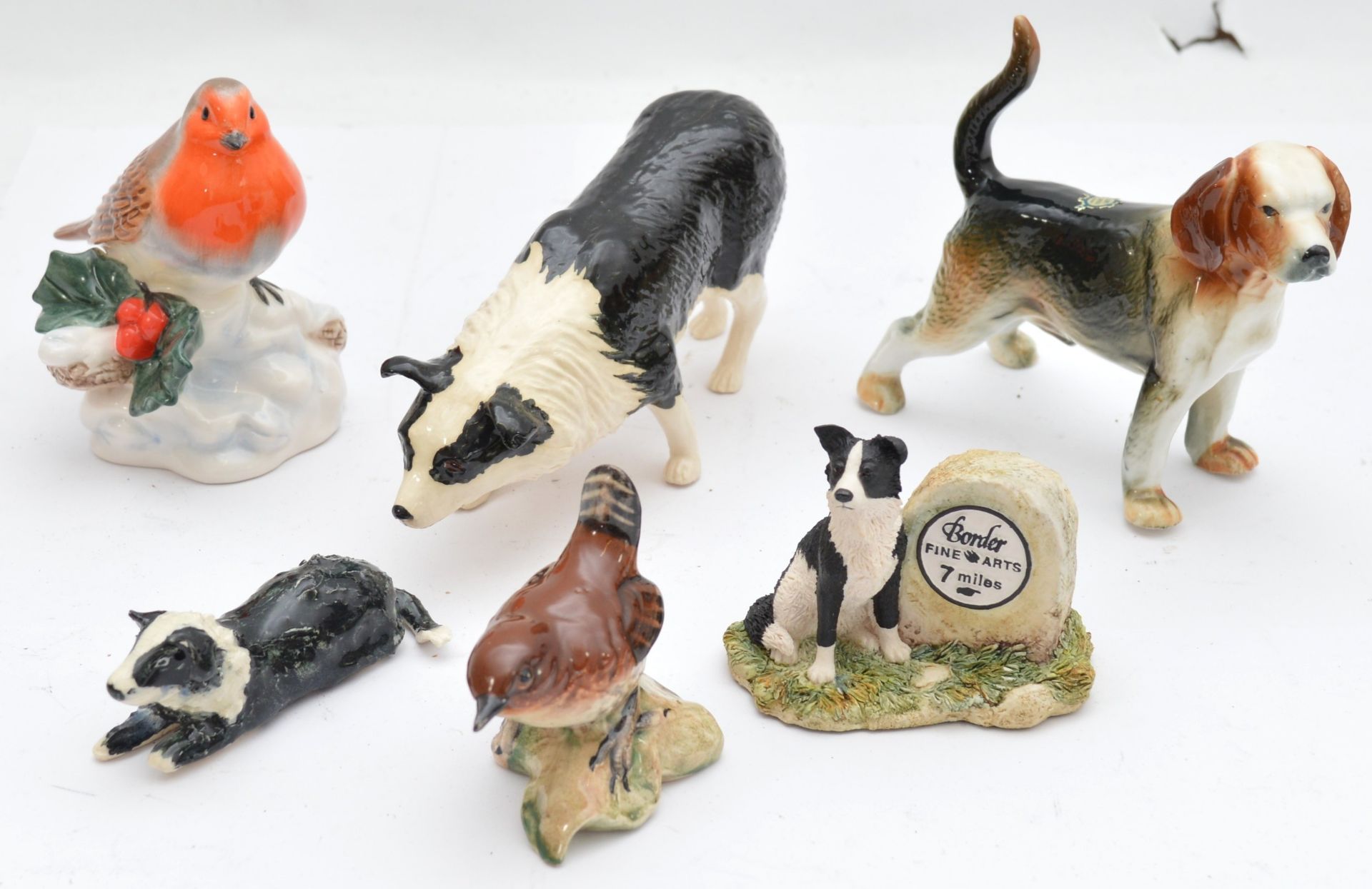 A group of six porcelain animal figurines, including a Beswick Robin, perched on a branch with holly