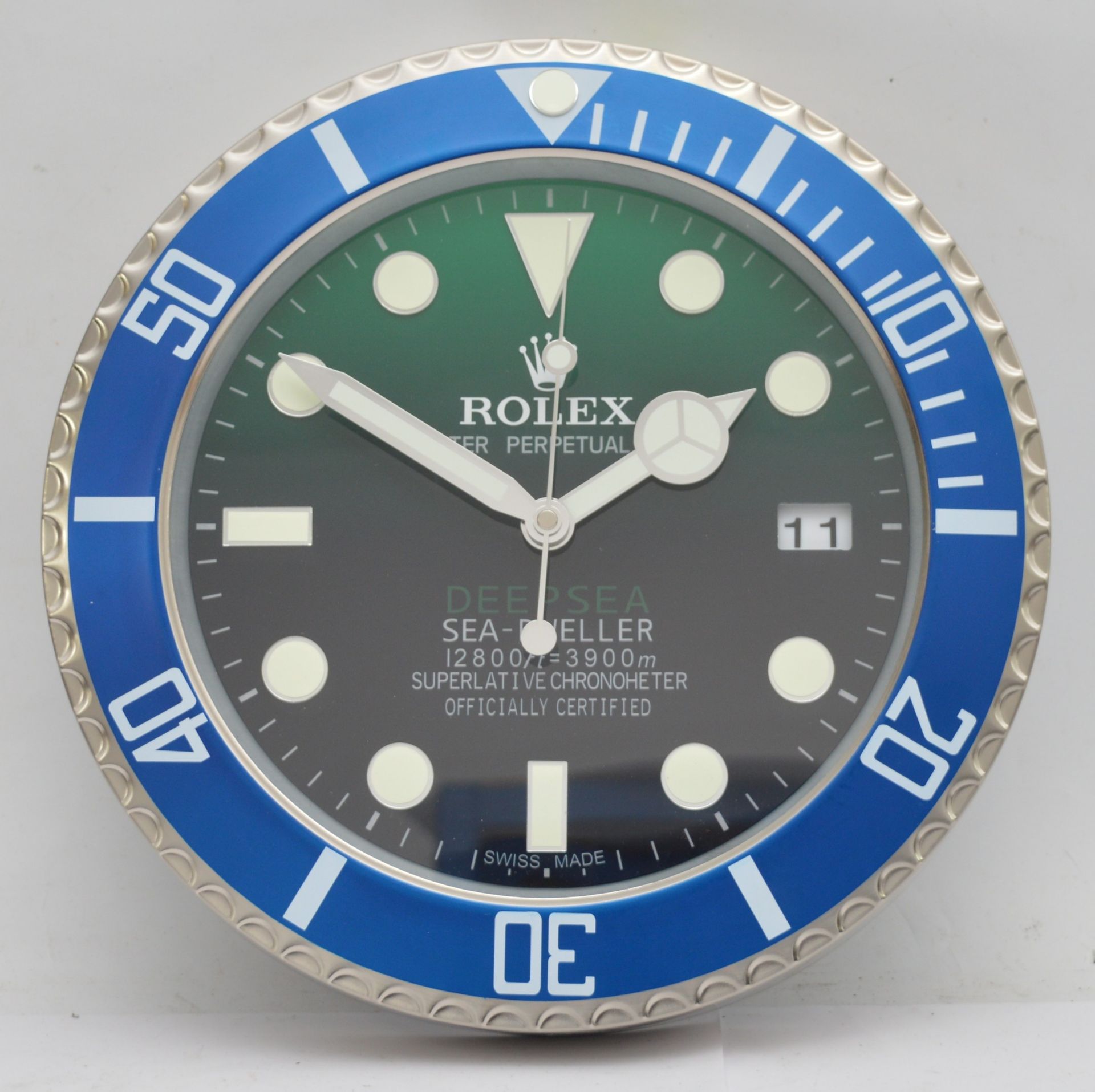 A 'Rolex' style advertising metal wall clock, green and black gradient dial with blue bezel, bearing