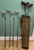A group of vintage golf clubs, including woods and irons in canvas and leather golf bag.