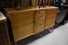 A vintage sapele sideboard of stylised design having central drawer section flanked by cupboards,