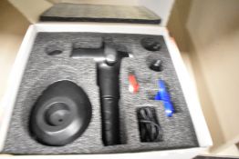 A cordless massage gun to aid with sore muscles includes various heads and stand etc.