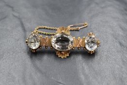 A yellow metal bar brooch having three aqua marine style stones in collared mounts on a decorative