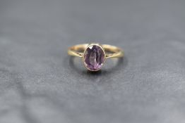 A 9ct gold amethyst ring having an oval stone in a collared mount to knife blade shoulders on a