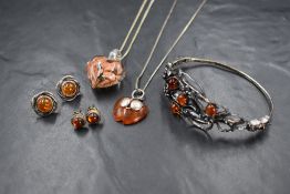 A silver amber set hinged bracelet, of pierced foliate design set with four circular amber