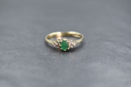 A 9ct gold emerald and diamond set ring, the central oval cut emerald flanked by three round cut