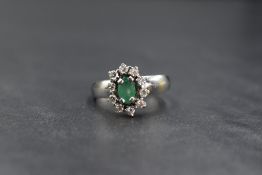A white metal emerald and diamond cluster ring stamped 18ct having an oval emerald, approx 0.5ct